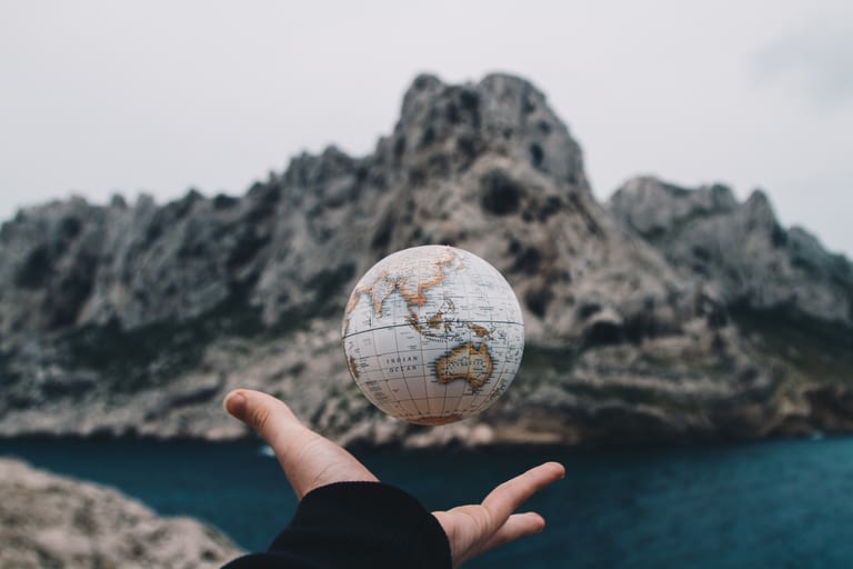 Hand tossing small globe in the air against a nature background